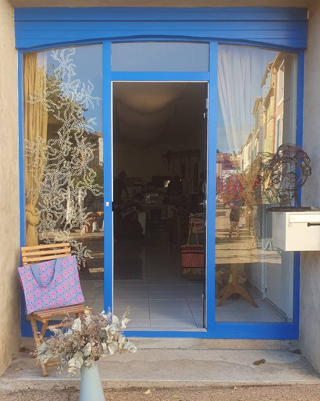 La devanture bleue de L’atelier de Cocotte, 36 place de la République à Leucate : vitrine décorée, chaise avec un cabas rose et bouquet d’eucalyptus devant la porte